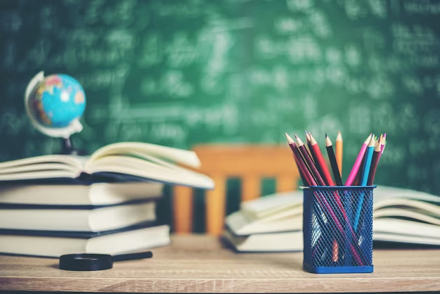 Table with pencils, books, a globe, and a blackboard with chalk-written lectures in the background.