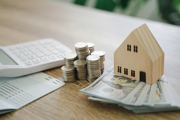 Coins, calculator, miniature house, and passbook on a table.