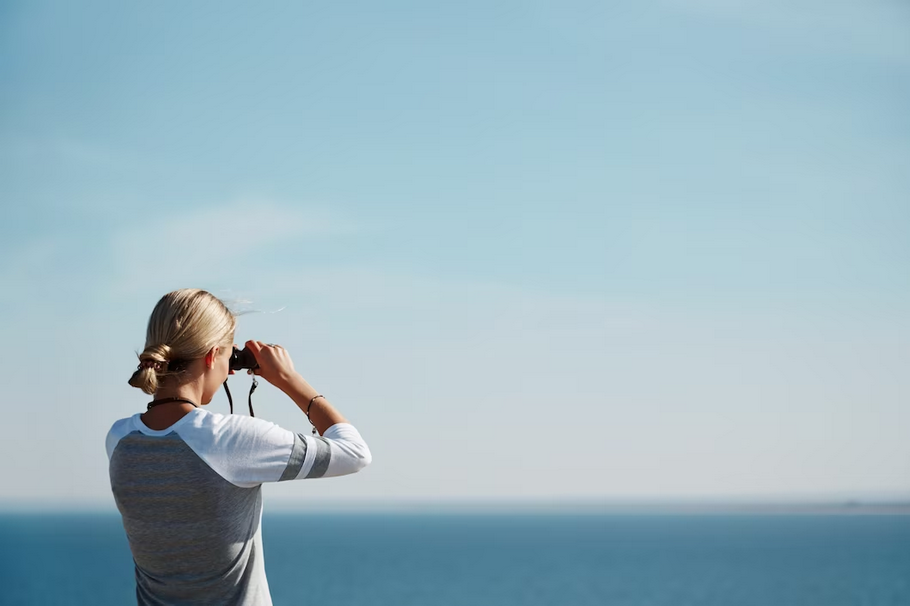 female using telescope with sea in the background