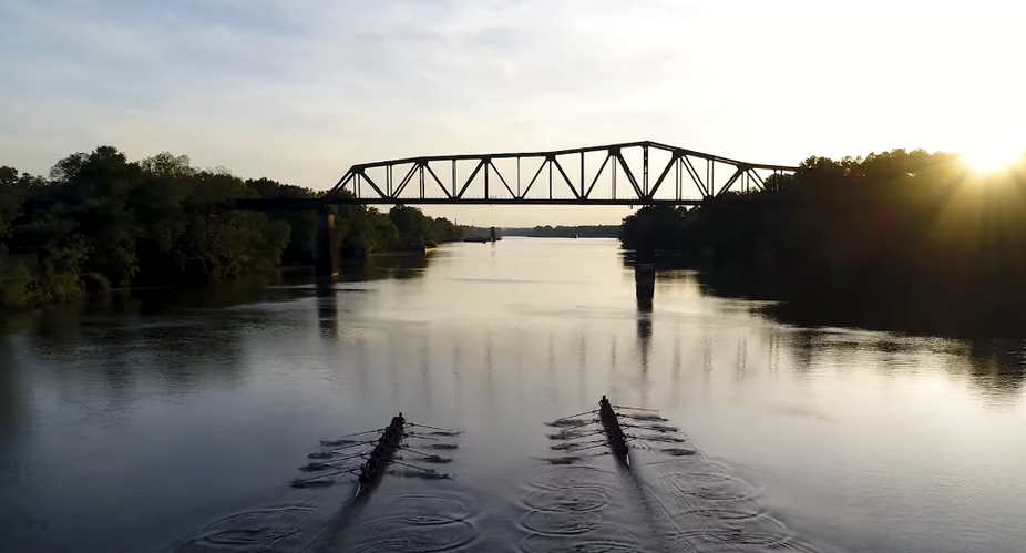 Silhouette of a bridge with sun and two boats on the river.