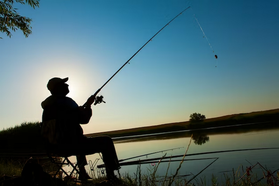 Silhouette of a cap-wearing man fishing.