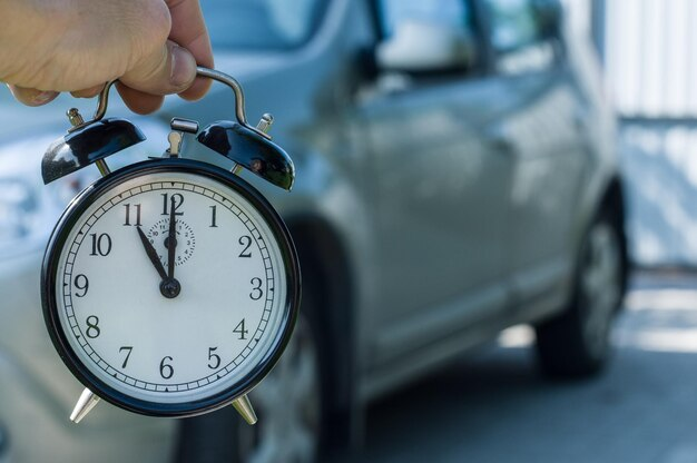 Hand holding a clock with a car in the background